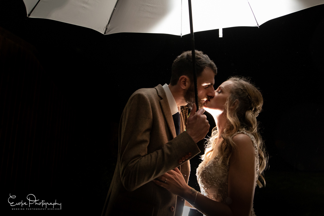 Bride & Groom kissing under an umbrella at their wet winter wedding at The Green in Cornwall 