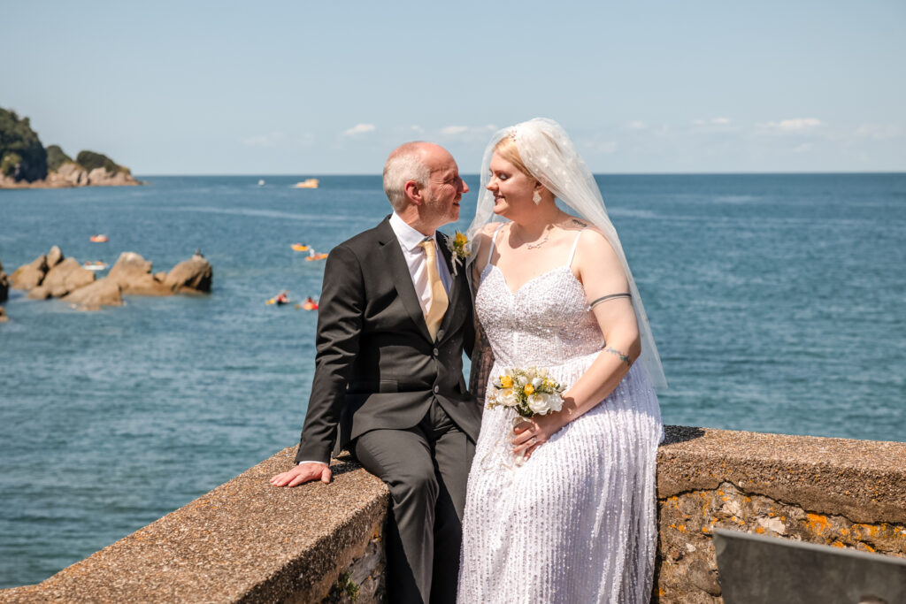 Groom Sat on Wall with Bride